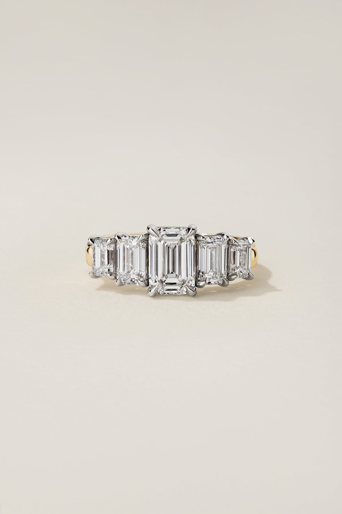 Nicci five-stone ring from the front: an emerald cut center diamond with four graduated emerald cut side stones in platinum, on an 18k yellow gold shank