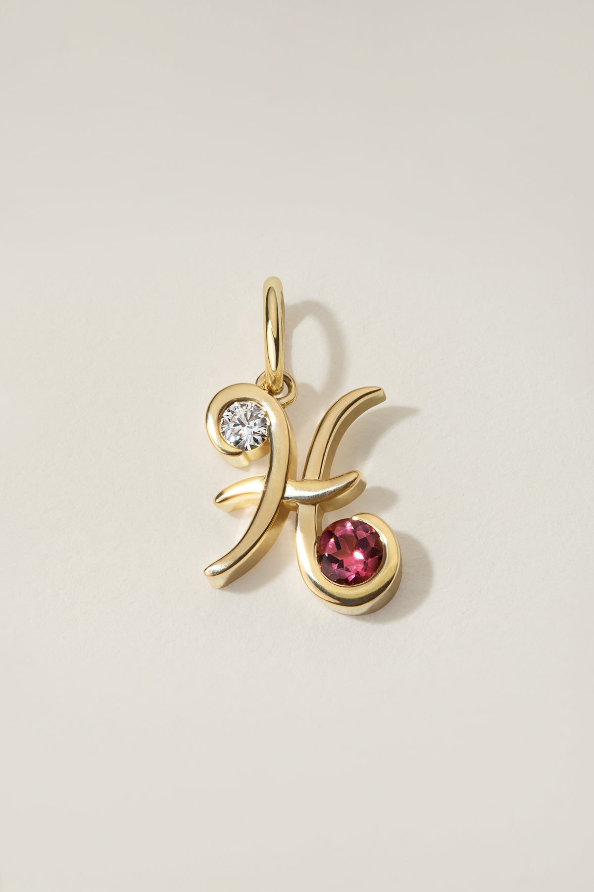 Two Stone Lettera Charm in 18k yellow gold, a script initial set with a diamond and a colored gemstone